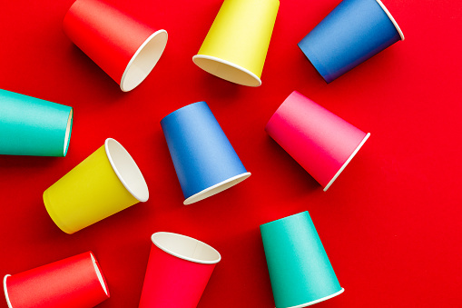 Close up image depicting a collection of colorful and recyclable eco friendly paper cups on a red background.