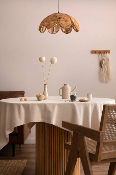 istock Boho and cozy interior of dining room with round wooden table, design chair, brown sofa, commode, pendant lamp, tea pot, decoration and elegant accessories. Stylish home decor. 1455755059