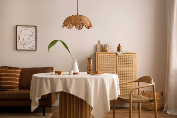 istock Boho and cozy interior of dining room with round wooden table, design chair, brown sofa, commode, mock up poster frame, pendant lamp, tea pot, decoration and elegant accessories. Stylish home decor. 1455755065