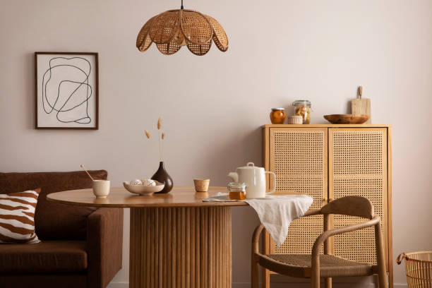 Boho and cozy interior of dining room with round wooden table, design chair, brown sofa, shelf, mock up poster frame, pendant lamp, tea pot, decoration and elegant accessories. Stylish home decor. Boho and cozy interior of dining room with round wooden table, design chair, brown sofa, shelf, mock up poster frame, pendant lamp, tea pot, decoration and elegant accessories. Stylish home decor. showcase interior dining room home decorating home interior stock pictures, royalty-free photos & images