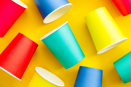 Close up image depicting a collection of colorful and recyclable eco friendly paper cups on a yellow background.
