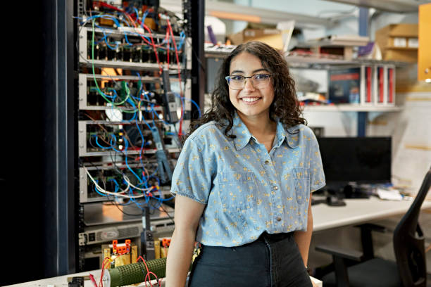 Portrait of early 20s female STEM student Waist-up view of casually dressed woman standing in electrical engineering lab and smiling at camera. Property release attached. education stage stock pictures, royalty-free photos & images