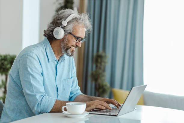 istock Mature man is using a laptop at the table in the living room 1455756665