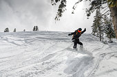 girl jumps with a snowboard from a hill, a springboard with snow, in the mountains against the background of trees
