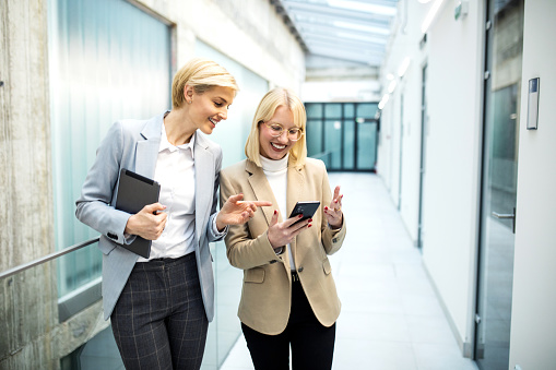 Two businesswoman woman walking thought business corridor and talking to each other about future plans of a company.