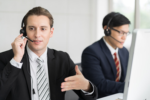 Male call center using headset support customer working in office with team as customer service operators. Group of male technical support operator customer service in the office