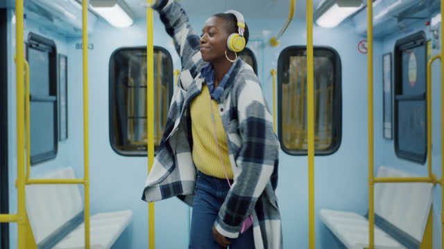 Young Stylish Black Woman Putting Headphones on and Dancing to the Beat of a Song in an Empty Tram. Carefree African American Teenager Enjoying her Time By Moving Along Happy Music. Slow Motion