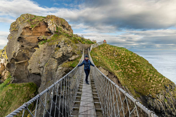 турист в восторге от пересечения веревочного моста каррик-а-реде на остров каррик-а-рид, графство антрим, северная ирландия, великобритания - cross autumn sky beauty in nature стоковые фото и изображения