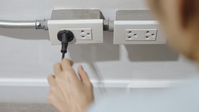 Woman plugging in an electric appliance to a wall socket for power.