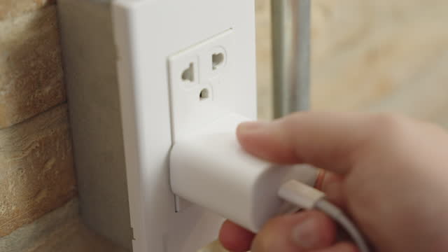 A hand pugging in a mobile phone charger into the brick wall power socket