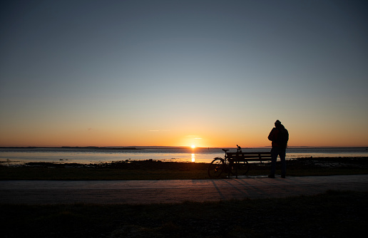 backpacker cyclist photographing and contemplating the sunrise in winter on the seaside street of galway ireland