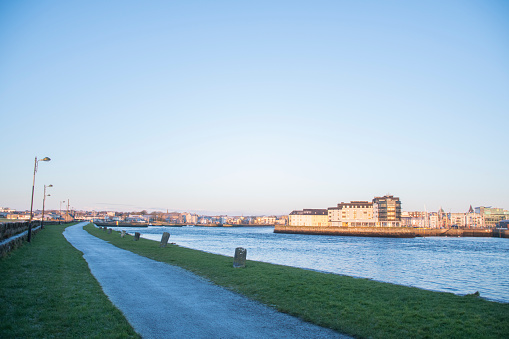 frozen pavement along the banks of the river Corrib in galway on a beautiful winter morning with the city in the background