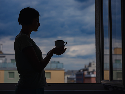 silhouette of a woman with a mug of tea on the background of the city.