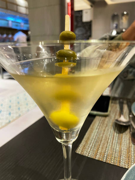 木の棒に4つのオリーブを添えたマティーニグラスの「汚れたマティーニ」カクテルドリンクの接写画像、ジン、ベルモット、オリーブ塩水、レストランの設定背景、前景に焦点を当てる - martini martini glass dirty martini olive ストックフォトと画像