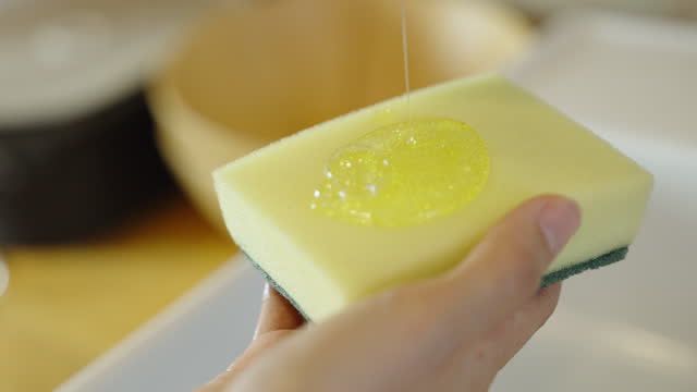 Woman's hand pouring dishwashing liquid on cleaning sponge.
