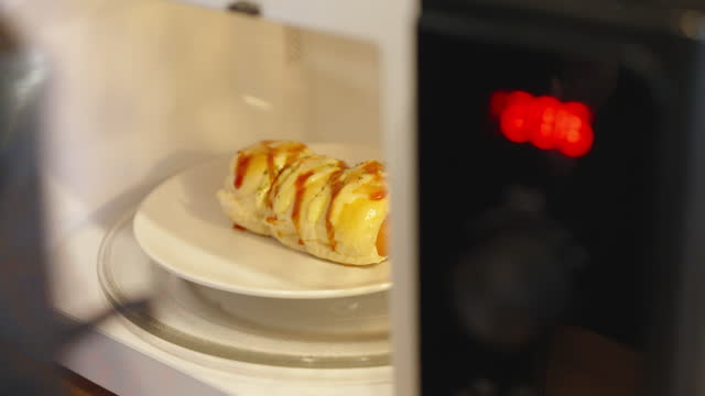 Sausage roll being taken off the microwave after finishing heating in the kitchen