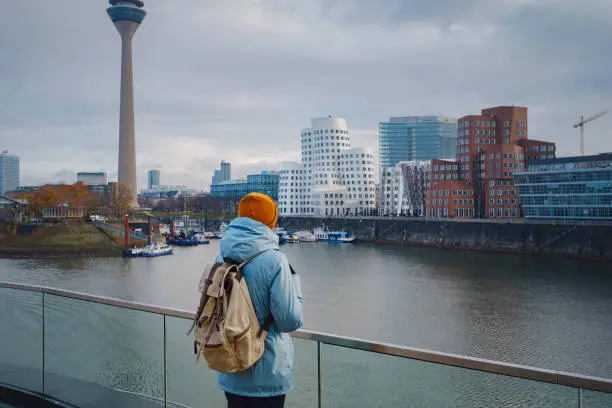 autumn or winter travel to Dusseldorf, Germany. young Asian tourist or student in blue jacket and yellow hat ( symbol of Ukraine) walks through sights of European city. beautiful view in the Media Bay