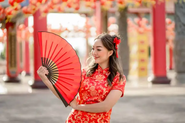 Happy Lunar Chinese new year festival. Beautiful lady wearing traditional cheongsam qipao costume holding fan in Chinese Buddhist temple.