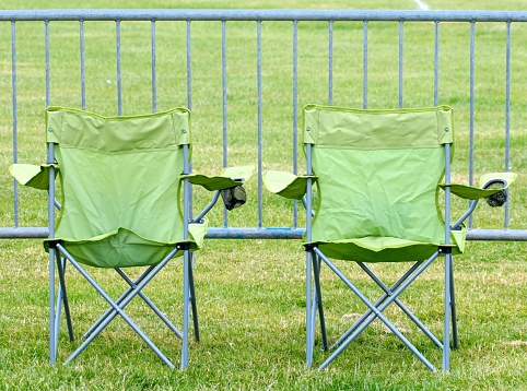View of the back of two green folding camping chairs placed in front of a metal barrier