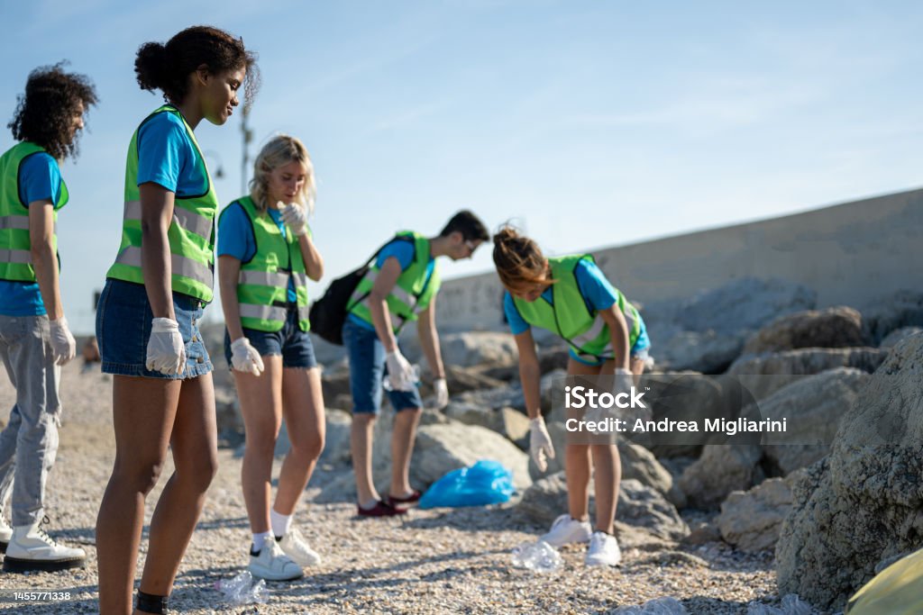 Female volunteer looking at the dirty coastline and starts cleaning, group of students work and pick up garbabe on beach 20-29 Years Stock Photo