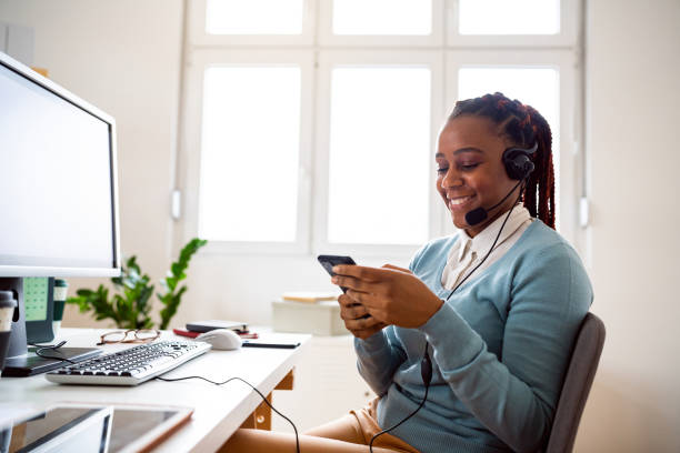 istock Young African ethnicity woman, a customer support specialist, using her phone while working at the office. 1455772102