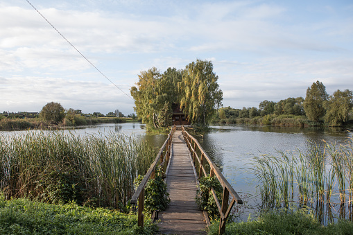 Fisher or Hunter house with wooden bridge on the middle of lake . Ukraine, Zhytomyr region