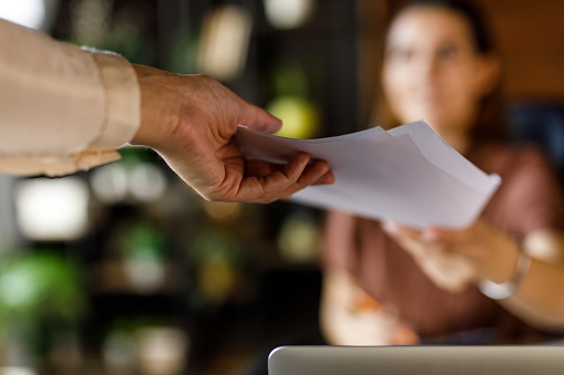 Close up shot of unrecognizable businesswoman handing a document to her coworker when co-working in a modern office space.