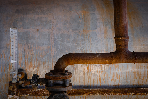 Old and rusty pipes and metal water tank with vertical gauge.