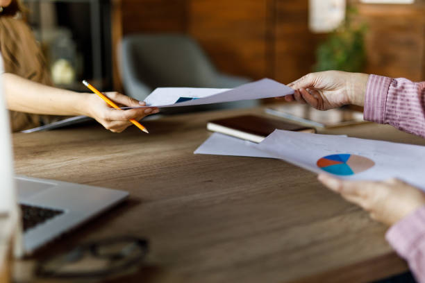 istock Two businesswomen exchanging documents over a desk 1455773863