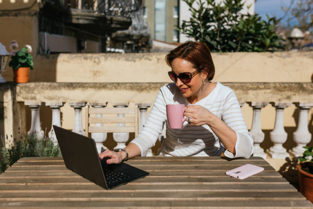 istock Woman using a laptop and drinking a cup of coffee while sitting outdoors in a terrace. 1455774222
