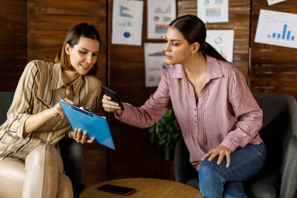 istock Two young businesswomen sitting at coffee table in a modern office, having a project briefing 1455774655