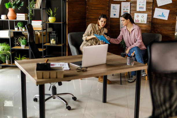 istock Two young businesswomen sitting at coffee table in a modern office, having a project briefing 1455774665