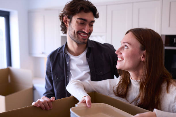 istock Young Couple Moving Into New Home Unpacking Boxes In Kitchen Together 1455775864