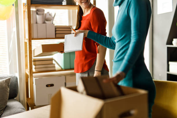 istock Two female entrepreneurs sorting and arranging cardboard boxes and packages at the office 1455776069
