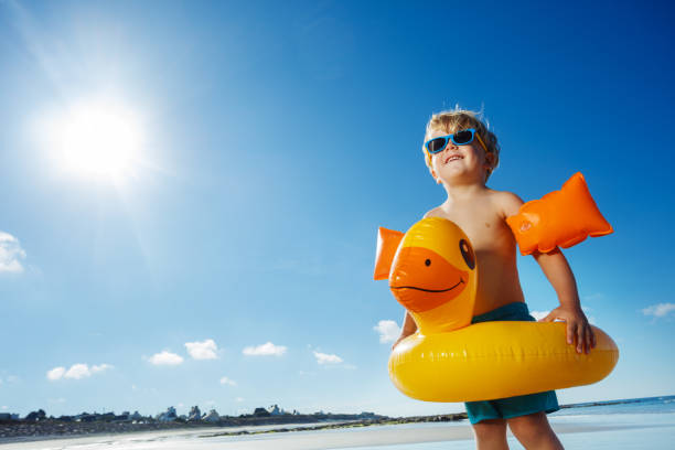 Little blond boy with inflatable yellow duck on ocean sand beach