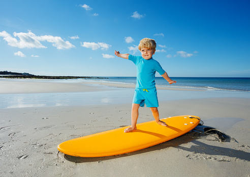 Cute little blond boy stand on the surfboard learning balance practicing surfing before going to the sea