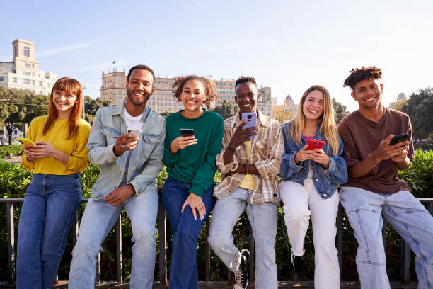 groupe multiracial d’amis utilisant un téléphone portable et regardant la caméra en souriant. - people in a row in a row human face smiling photos et images de collection