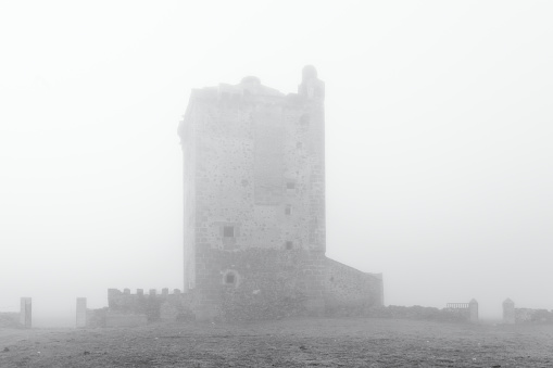 Tower of the Mogollones. Landscape with a medieval tower shrouded in fog. Extremadura. Spain.