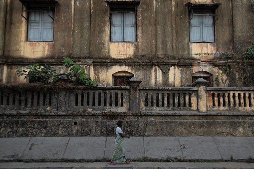 A person walks in front of a brown and overgrown building in the center of Mawlamyine. The small city is located south of the capital of Yangon and is surrounded by small rural communities. Mawlamyine, Myanmar