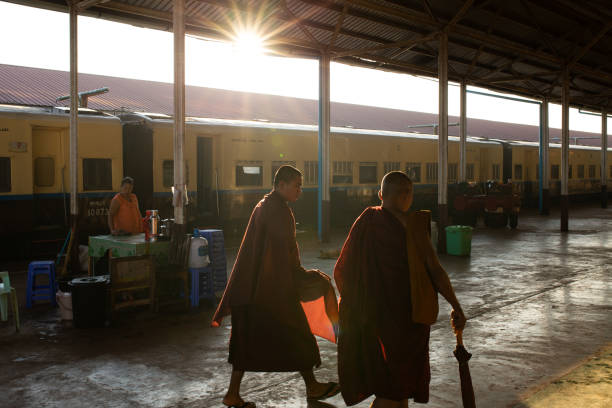 монахи идут через утренний свет на старом железнодорожном вокзале - мьянма - burma railway стоковые фото и изображения