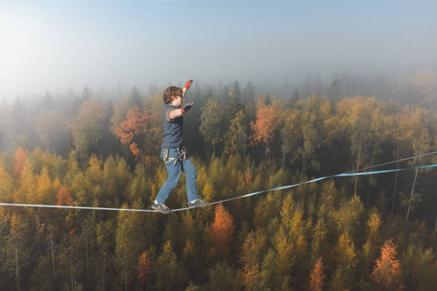 Tightrope walker against the backdrop of a stunning atmospheric forest Slackline at high altitude. A man walks on a rope against the backdrop of a foggy autumn forest highlining stock pictures, royalty-free photos & images