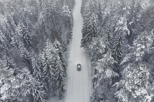 The car rides on a winter road in a snowy forest. Air view. Topic of automobile transport