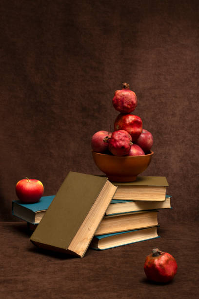 Still life with apples and pomegranates, a brown plate and a stack of books