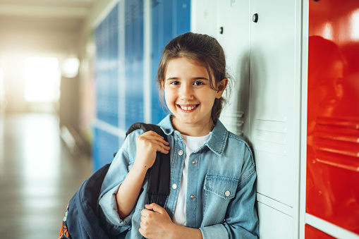 Portrait of happy student with backpack standing by locker in corridor