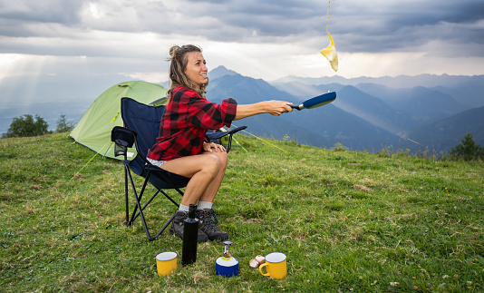 Female hiker by her tent preparing lunch in the mountain. Healthy Lifestyle and nature concept.