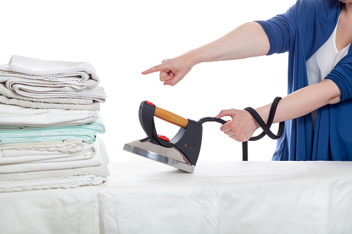 A woman jokingly commands bite to ironing a pile of laundry while holding the iron by the electric wire