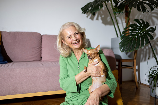 Pretty senior caucasian woman playing with her dog at home looking at camera.