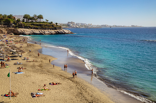 Costa Adeje, Tenerife, Spain - February 8, 2019: View of the beach with people in a popular resort in southern coast of the island, Canary Islands.