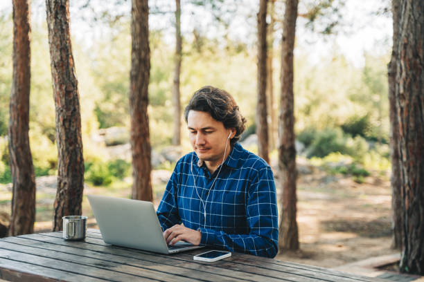 Happy cheerful man with a laptop sitting outdoors in nature forest park. Freelancer with computer typing, blogging, browsing in vacation in mountains. Freelance, distance work concept. hombre alegre y feliz con una computadora portátil sentado al aire libre en el parque forestal natural. freelancer con computadora mecanografiando, blogueando, navegando en vacaciones en montañas. freelance, concepto de trabajo a distancia