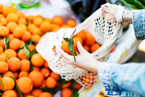 Young adult woman buying tangerine at farmer's market with textile bag